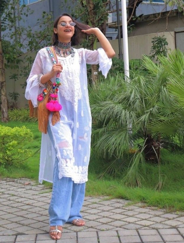 A Young Lady holding colorful bag and Style a White Chikankari Kurti, paired with Baggy Jeans and sunglasses with jwelleries. 