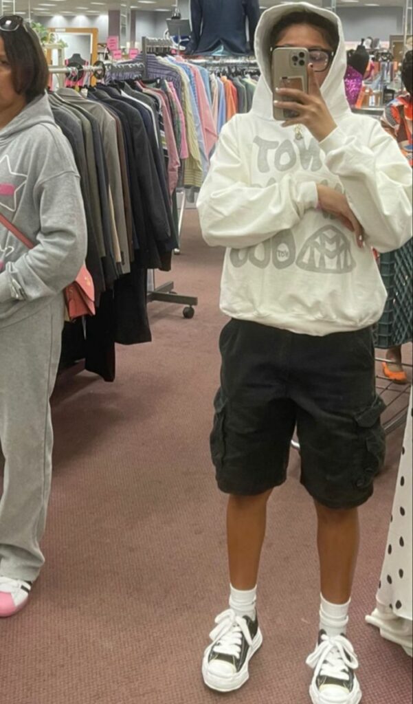 posing a young man to style a hoodie with half cargo pants standing in clothes store. 