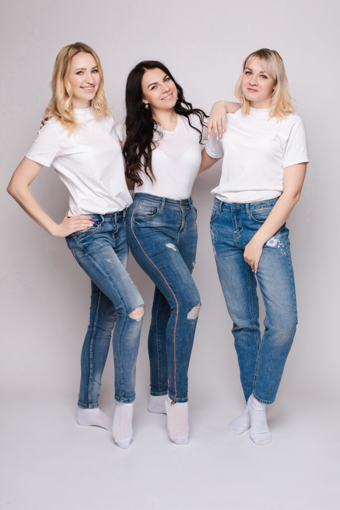Three beautiful women wearing white shirt and ripped jeans and posing on isolated background. 